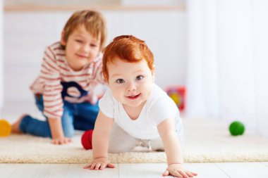 Evde yerde sürünen mutlu kızıl saçlı erkek bebek portresi.