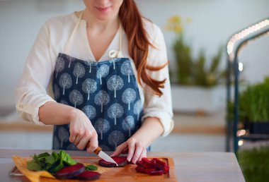 Mutfakta organik çiğ salata için pancar ve ıspanak yaprakları kesen kadın. Arka planda mikro yeşil tarım ve sağlıklı vejetaryen besin.