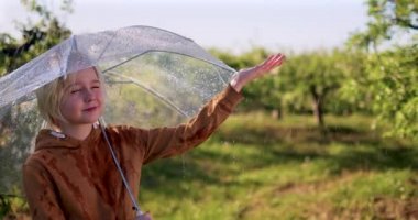 Mutlu genç çocuk güneşli elma bahçesinde ılık yaz yağmurunun tadını çıkarıyor.