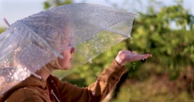 Güneşli yaz gününde bahar bahçesinde şemsiyeden düşen yağmur damlalarını yakalayan neşeli çocuk.