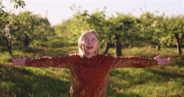 幸せな少年は晴れたリンゴ園で暖かい夏の雨を楽しんでいます — ストック動画
