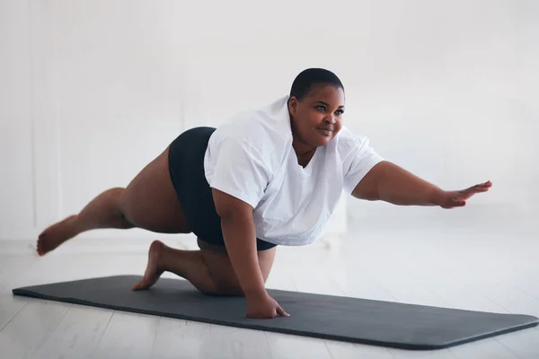 beautiful plus size woman exercising on sport mat at home, lifting legs and arms up