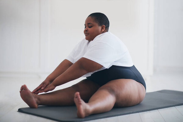 young plus size woman does stretching exercises on sport mat at home, muscules warm-ups