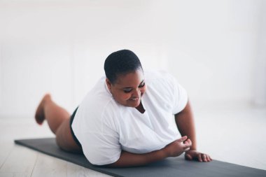 Mutlu, genç ve iri bir kadın evde spor paspası üzerinde esneme egzersizleri yapıyor.