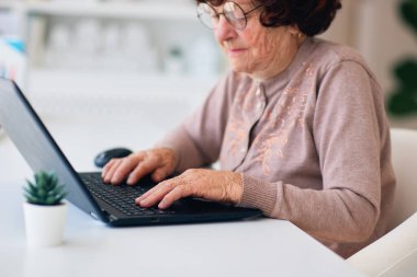 Dizüstü bilgisayar kullanan, interneti karıştıran, evdeki masada e-posta yazan yaşlı bir büyükanne.