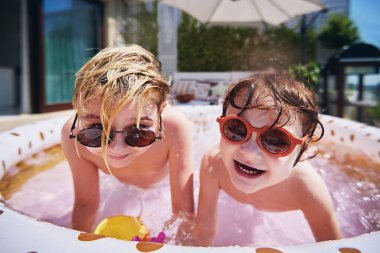 Heyecanlı çocuklar güneşli bir yaz gününde evdeki terasta şişme yüzme havuzunda eğleniyorlar.