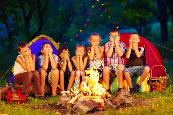 Funny kids with painted faces on hands sitting around camp fire — Stockfoto