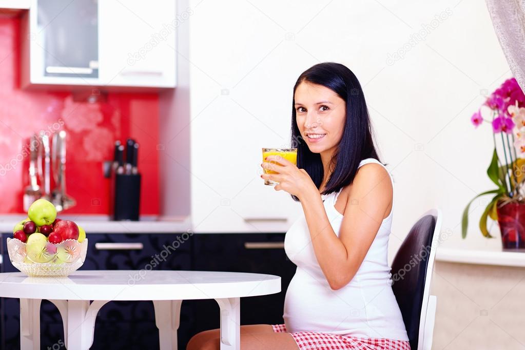 Pregnant woman drinking fresh juice in kitchen — Stock Photo