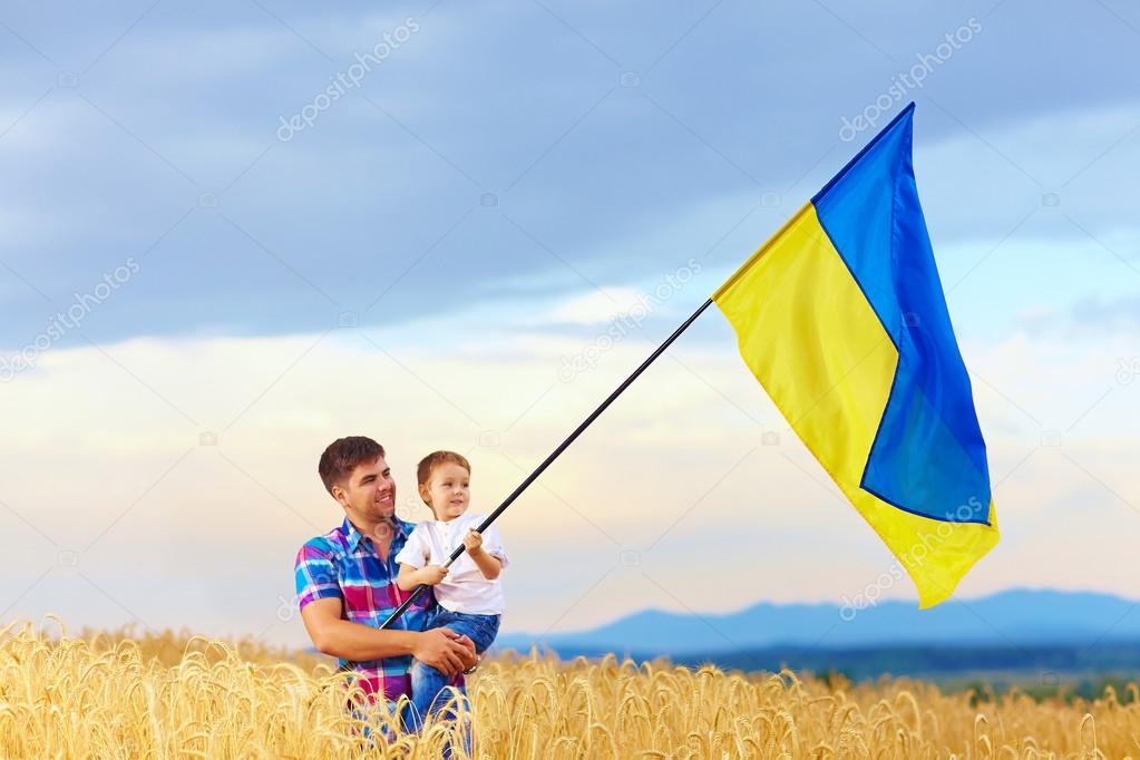 father and son waving ukrainian flag on wheat field