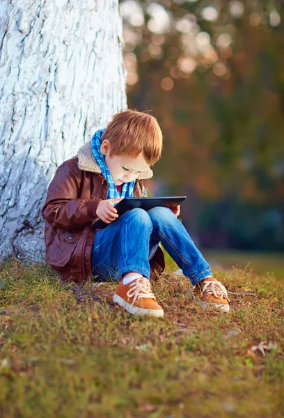Feliz chico con estilo jugando en la tableta de medios en el parque de la ciudad —  Fotos de Stock