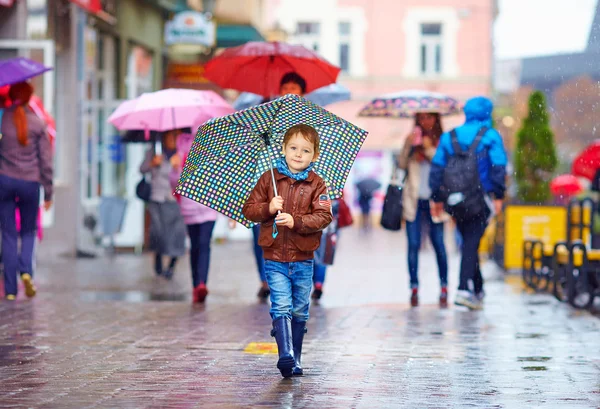 Netter Junge mit Regenschirm läuft auf überfüllter Stadtstraße — Stockfoto