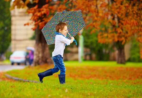 Милый мальчик наслаждается осенним дождем в городском парке — стоковое фото