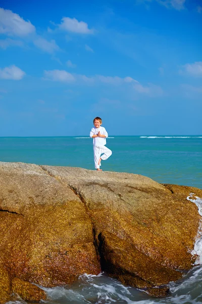 Ragazzo carino praticando yoga sulla roccia nel mare — Foto Stock