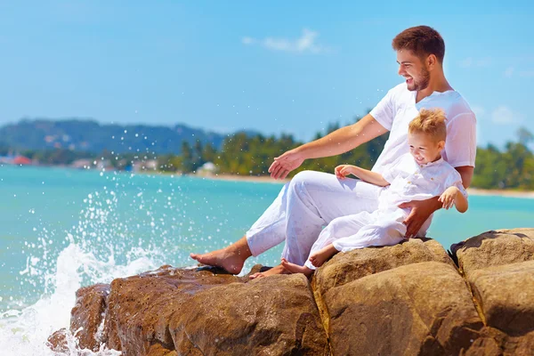 Wasser plätschert auf lachendem Vater und Sohn an felsiger Küste — Stockfoto