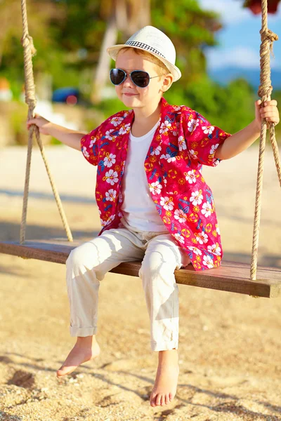 Cute stylish boy on swings at the beach — Stock Photo, Image