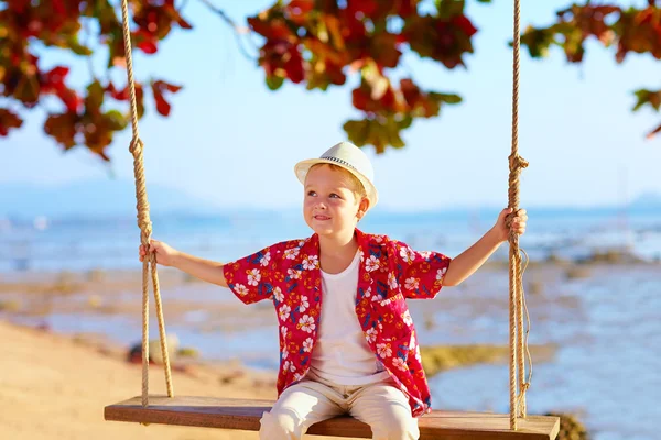Cute stylish boy on swings on the beach — Stock Photo, Image