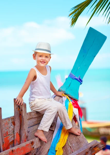 Słodkie dziecko, chłopiec siedzi na starej łodzi na tropikalnej plaży — Zdjęcie stockowe