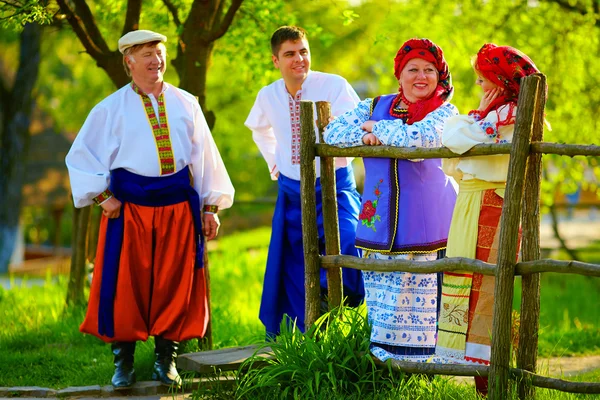 Heureuse famille ukrainienne en costumes traditionnels parlant près de la clôture en bois — Photo