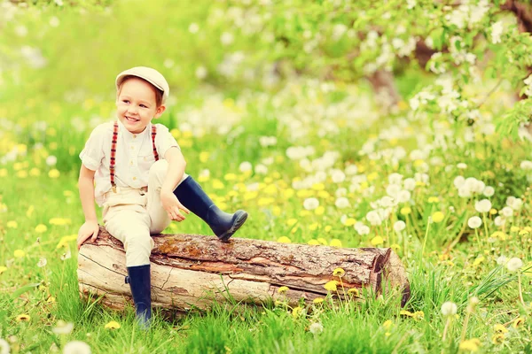 Menino feliz bonito sentado no toco de madeira no jardim de primavera — Fotografia de Stock