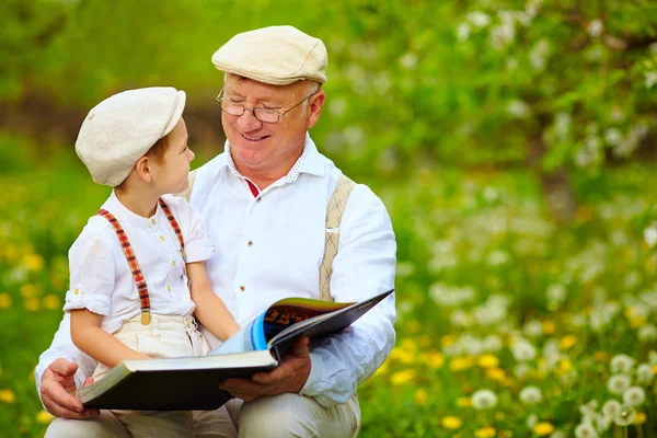 Abuelo con nieto leyendo libro en jardín de primavera — Foto de Stock