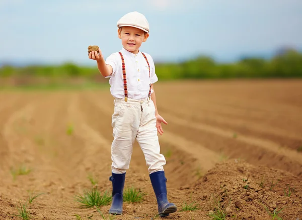 Cute little farmer on spring field  holding earth clod — Stock Photo, Image