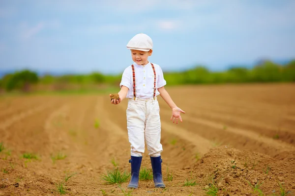 Cute little farmer on spring field  holding earth clod — Stock Photo, Image