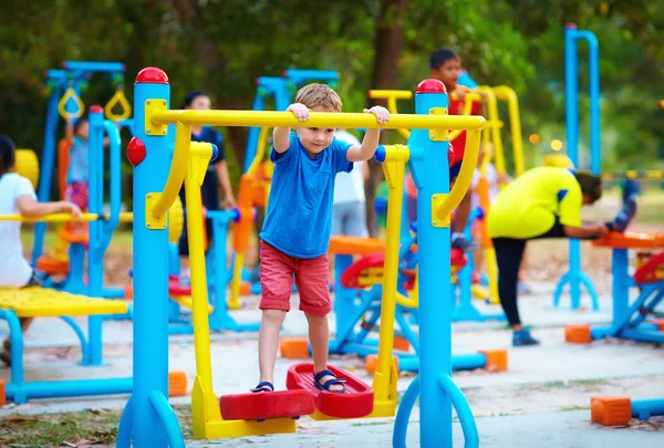 Cute kid, boy exercising on sport ground with other people on background — Stock Photo, Image