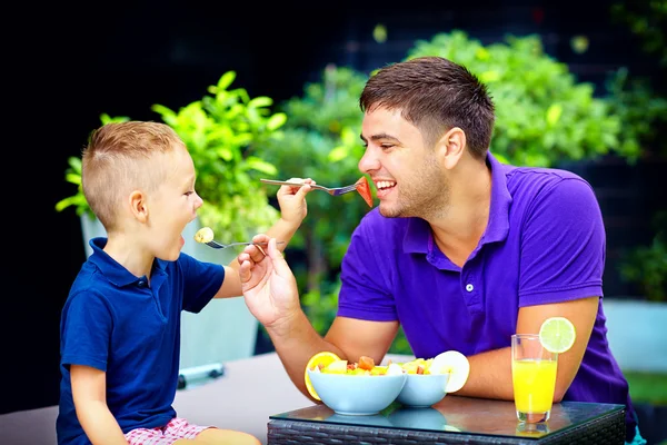 Joyful father and son feeding each other with tasty fruit salad — Stock Photo, Image
