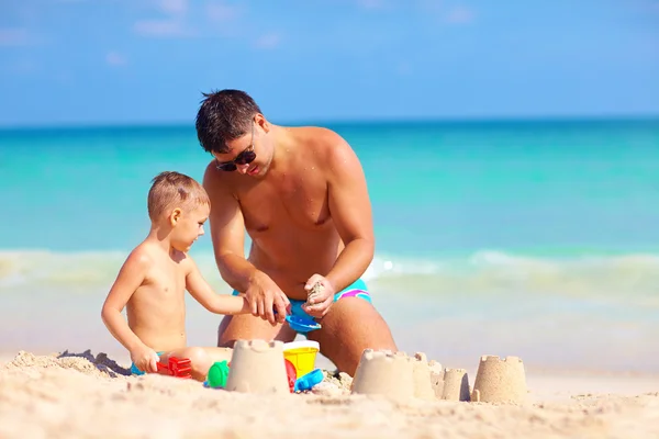 Baba oğlu yaz sahilde kum kale inşa yardımcı olur. — Stok fotoğraf
