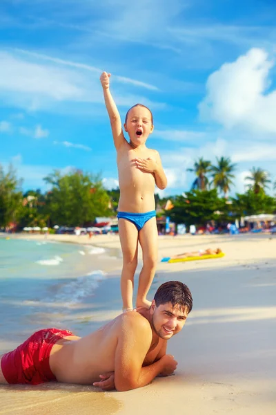 Игривый ребенок, притворяющийся Статуей Свободы, с отцом на тропическом пляже — стоковое фото