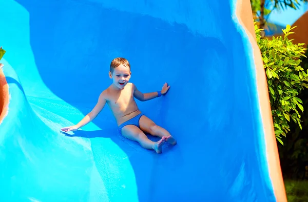 Bambino felice scorrevole nel parco acquatico tropicale — Foto Stock