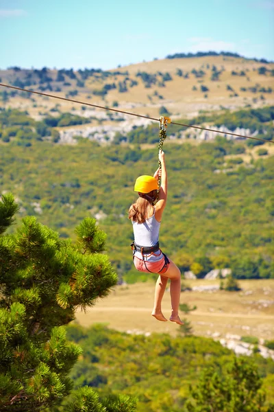 Young woman flying down on zipline in mountain, extreme sport — Stock Photo, Image