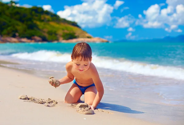 Bambino sorridente che gioca nella sabbia sulla spiaggia dell'isola tropicale — Foto Stock