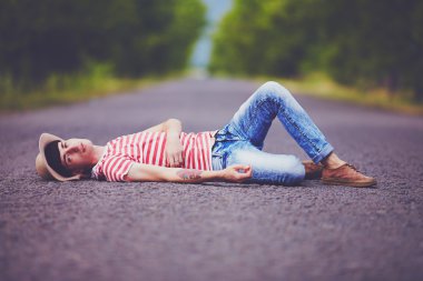 young stylish boy lying on summer road