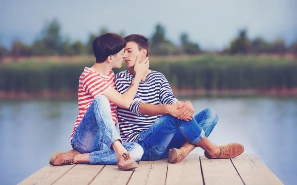 Gay couple kissing on wooden pier at riverbank — Stock Photo, Image