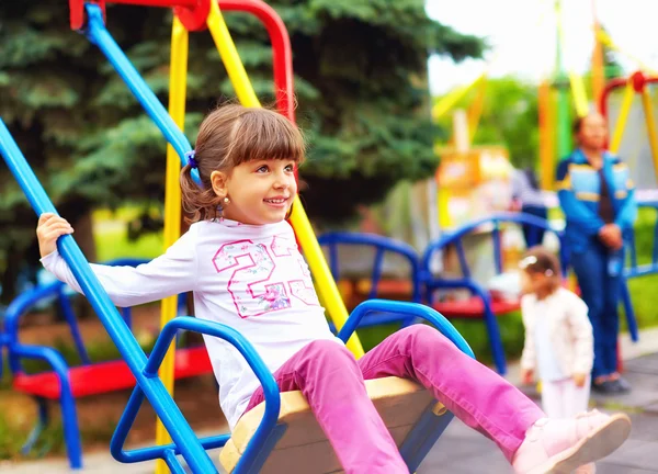 Linda chica feliz, niño se divierte en columpios en el patio de recreo — Foto de Stock