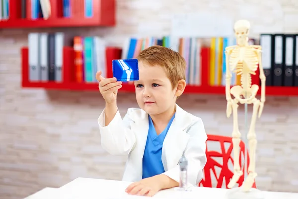 Милий хлопець грає лікаря, дивлячись на рентгенівське зображення ноги — стокове фото