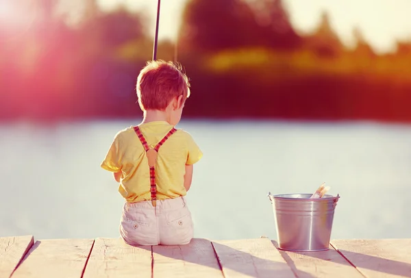 Schattige kleine jongen bij zonsondergang op een vijver vissen — Stockfoto