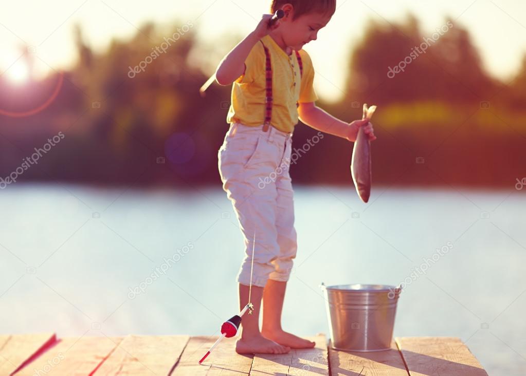 defocused image of little boy caught a fish on the hook, on pond at sunset