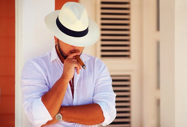 Confident handsome man smoking cigar, while leaning on the wall — Stock Photo, Image