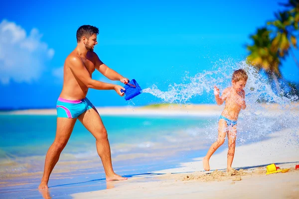 Šťastný otec šplouchání vody na smějící se synem, letní prázdniny — Stock fotografie