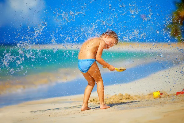 Water splashes on excited kid boy, on tropical beach — Stock Photo, Image