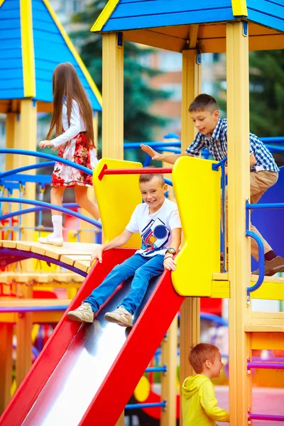 Groep van gelukkige jonge geitjes glijden op kleurrijke speeltuin — Stockfoto