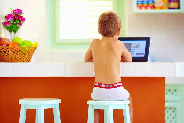Ung liten pojke tittar på video via internet, medan du sitter i köket på morgonen — Stockfoto