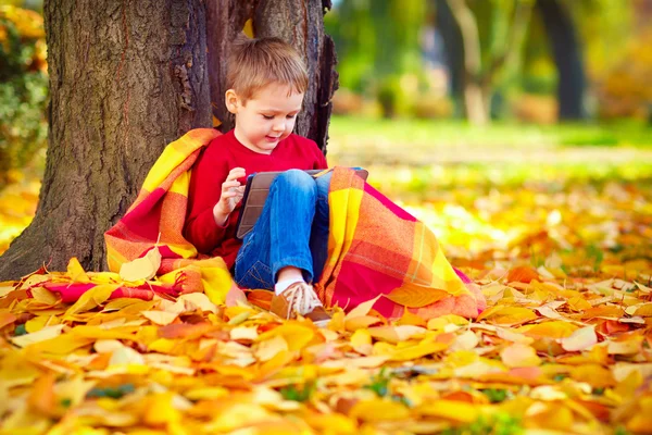 Schattige jongen met tablet zitten in herfst park — Stockfoto