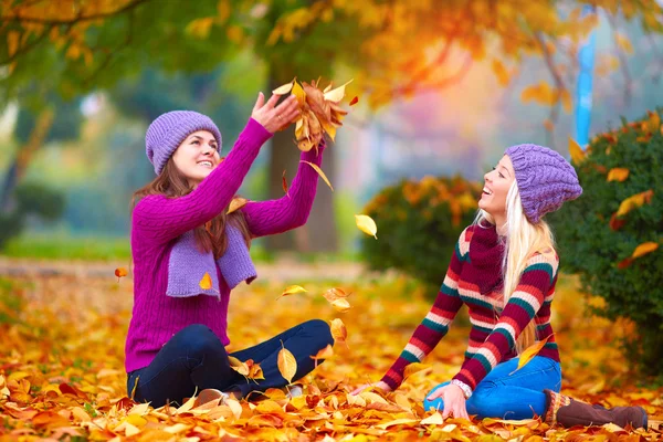 Pretty girls, friends having fun in colorful autumn park, tossing the leaves up — Stock Photo, Image