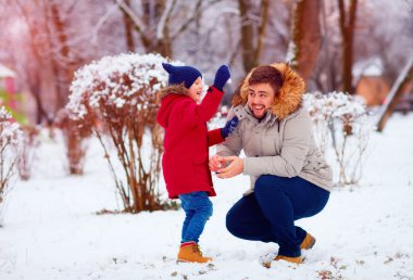 active father and son playing snowballs in winter park clipart