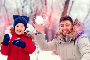 active father and son playing snowballs in winter park clipart