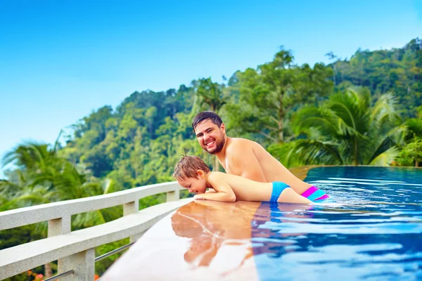 Feliz padre e hijo relajándose en la piscina infinita en la isla tropical —  Fotos de Stock