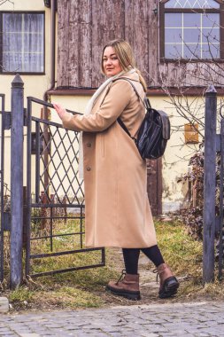 Parktaki güzel beyaz bir kadının portresi, bej rengi kaşmir ceket, siyah deri sırt çantası, günlük sokak tarzı kıyafet, günlük moda.